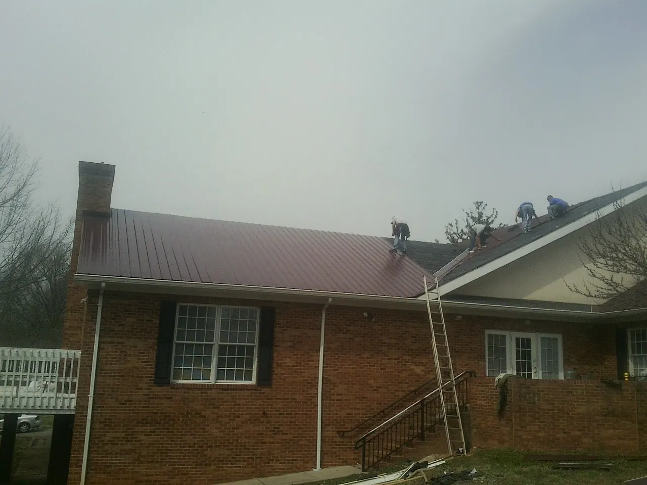 Crew setting red metal roofing panels on a brick home in Dover